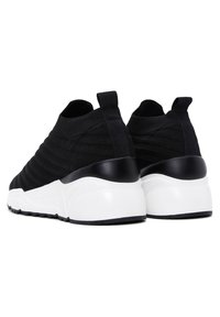 Pair of black knit slip-on sneakers with white chunky soles and black heel tabs, shown from the back on a white background.