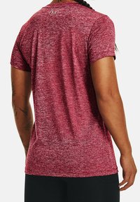 Person wearing a maroon speckled short-sleeve athletic shirt with a small logo on the upper back, shown from behind.