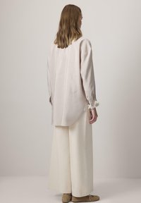 Blusa de manga larga rosa claro con un corte holgado, que presenta una tela texturizada, puños partidos con acentos, combinada con pantalones de pierna ancha color crema.
