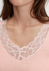 Top rosa a costine con un ampio e delicato scollo in pizzo con motivi floreali. La texture liscia aumenta la morbidezza complessiva del capo.