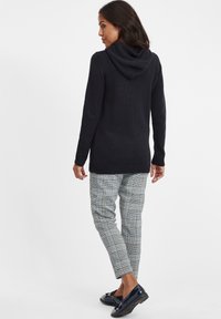 Czarna dzianinowa bluza z kapturem o luźnym kroju, z szwem z tyłu i ściągaczami, zestawiona z kraciastymi spodniami w odcieniach niebieskiego, szarości i bieli.