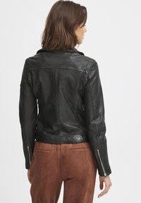 Black leather jacket with a fitted design, featuring zipped cuffs and a notched collar. Smooth texture with visible seams on the back.