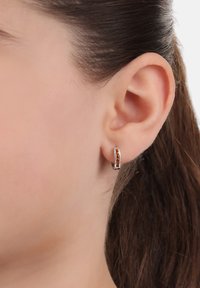 Orecchino a cerchio in argento con una fila di gemme arancioni, che mostra un design elegante e una texture liscia, indossato all'orecchio di un modello.