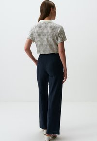 Faktura biała z granatowymi paskami krótka bluzka w połączeniu z granatowymi spodniami o wysokim stanie. Modelka nosi białe sandały na słupku.