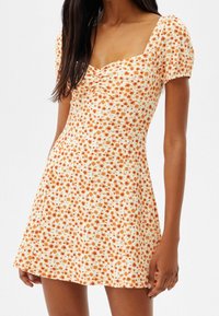 Robe fleurie avec manches courtes bouffantes, corsage froncé et jupe évasée. Fond blanc avec motifs floraux orange partout.