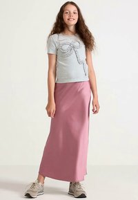 T-shirt gris à manches courtes avec un motif en relief en forme de nœud et une jupe longue rose. Porté avec des baskets de sport beige. Design simple et décontracté.