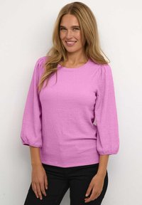 Top rosa testurizzato con scollo rotondo e maniche a sbuffo, abbinato a pantaloni neri. Presenta un tessuto morbido e stropicciato e una silhouette aderente.