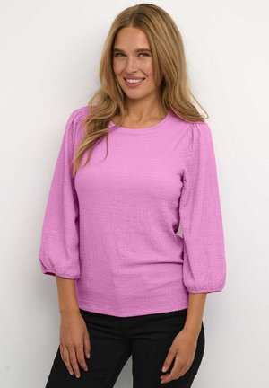 Top texturizado rosa con cuello redondo y mangas abullonadas, combinado con pantalones negros. Presenta una tela suave y arrugada y una silueta ajustada.