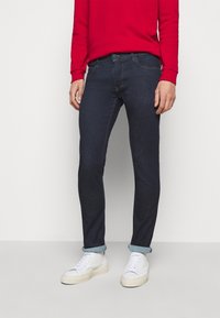 Mörkblå denimjeans med slim fit, uppvikt fåll, framfickor och kontrasterande sömmar. Matchas med vita sneakers och en röd sweatshirt.