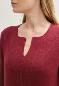 Burgundy knit sweater with a v-shaped neckline. Soft texture, fitted silhouette, and line details enhancing the design. Long sleeves.