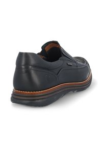 Zapato negro de piel sin cordones con acentos en tono marrón, punta redondeada, paneles elásticos en los laterales y suela de goma texturizada. Detalles de costura visibles.