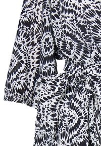 Rochie din material cu un model alb-negru, cu mâneci scurte, talie strânsă cu o fundă și un design fluid.