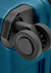 Blauer Koffer mit einer schwarzen drehbaren Rolle an der Ecke. Die Oberfläche ist glatt mit einer leichten Struktur. Das Raddesign zeigt eine kreisförmige Basis und geriffelte Akzente.