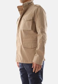 Giacca leggera beige con collo alto, multiple tasche, chiusura con bottone e dettagli di cucitura visibili; texture liscia.