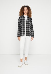 Camisa de flanela aos quadrados em preto e branco, corte confortável, com botões; combinada com calças brancas justas e ténis brancos. Textura suave no geral.