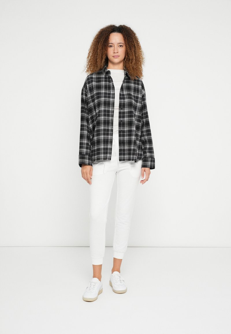 Camisa de flanela aos quadrados em preto e branco, corte confortável, com botões; combinada com calças brancas justas e ténis brancos. Textura suave no geral.