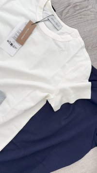 White and navy cotton t-shirts laid flat. The white shirt has a tag labeled "organic cotton," round neckline, and short sleeves.
