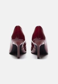 Scarpe con tacco alto bordeaux lucido con punta affilata e silhouette slanciata. Presentano un tacco a spillo stretto e una superficie liscia.