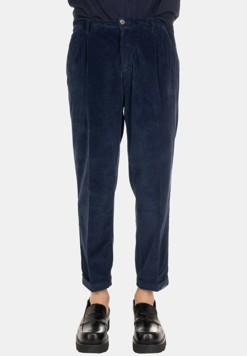 Pantaloni di velluto a coste blu navy con superficie strutturata, caratterizzati da una vestibilità comoda, pieghe frontali e chiusura con bottone. Orli arrotolati che lasciano scoperta la caviglia.