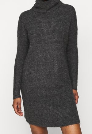 Mørkegrå ribstrikket sweaterkjole med lange ærmer og en løs høj krave båret af en stående person.