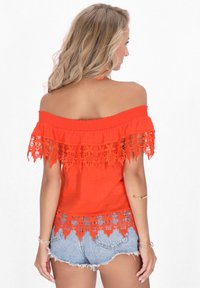 Top rosso scollato con pizzo e tessuto intrecciato, abbinato a pantaloni shorts in denim. Presenta un collo elastico e dettagli in pizzo intricati.