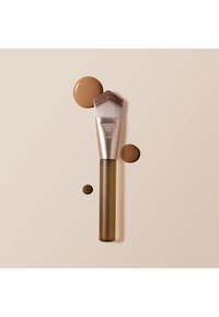 Skråstilt sminkekost med brun håndtak, merket RT 139, omgitt av tre dråper flytende foundation i forskjellige størrelser på beige bakgrunn.