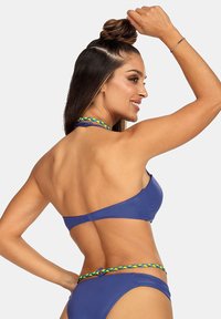 Niebieski strój kąpielowy składający się z góry na halter oraz majtek hipsterskich. Udekorowany kolorowym plecionym paskiem. Gładka tekstura i dopasowany krój.