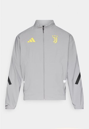 Siva vjetrovka s žutim Adidas logotipom i oznakom Juventusa, s crnim detaljima, patentnim zatvaračem sprijeda i elastičnim manšetama.