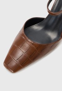 Valkoinen nahkainen slingback-kengä, jossa on krokotiilitekstuuri, teräväkärkinen ja ohut nilkkahihna, jossa on tyylikäs musta sisustus.
