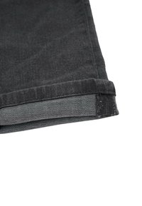 Svart denimbyxa med uppvikt fåll, där en grå innertyg är synligt. Tyget har en subtil textur och en lätt lyster.