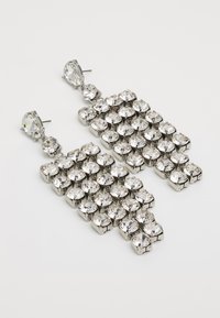 Sølvfargede dråpeøreringer med flere runde klare rhinestones i et rutenettmønster, med en teksturert metallbase.