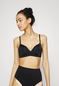 Black wireless bra with a smooth, matte finish, plunging neckline, and adjustable straps, paired with high-waisted black briefs.