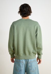 Green cotton sweatshirt with a crew neck, ribbed cuffs, and hem. The back shows a relaxed fit, paired with light blue denim shorts.