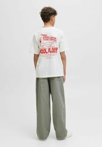 Witte t-shirt met rode grafische print van een eend en tekst over het repareren van zwembandjes. Losvallend, gecombineerd met lichtgroene wijde broek.