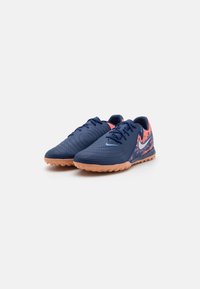 Marineblauwe sportschoenen met een tekstuur bovenkant, oranje accenten en een gumrubberen zool, voorzien van vetersluiting en een Nike-logo op de zijkant.