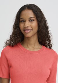 T-shirt corail en coton tricoté avec manches courtes et encolure ronde, présentant une texture lisse et un détail discret de côtes.