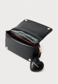 Μαύρη δερμάτινη τσάντα ώμου με χρυσό κούμπωμα, εσωτερικό με κόκκινο σχέδιο, κλείσιμο με κουμπί και δερμάτινο μπρελόκ σε σχήμα καρδιάς που γράφει "LOVE MOSCHINO."