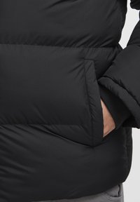Sort polstret jakke med en rummelig sidelomme og en stilfuld, glat finish. Blød tekstur med et let, isoleret design.