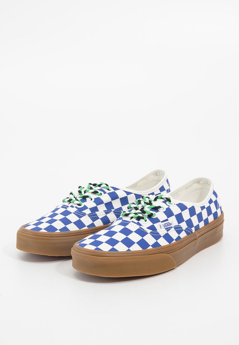 Baskets en toile à motif carrelé bleu et blanc avec des lacets verts, dotées d'une semelle en caoutchouc marron et d'un logo sur le côté.