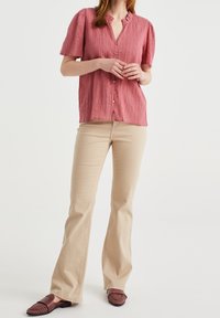 Rosa strukturerad kortärmad blus med en urtagning vid kragen och framknappar, matchad med beige utsvängda byxor och vinröda vävda slip-ons.