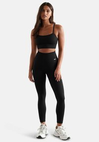 Set di activewear nero a coste con top corto a spalline sottili e leggings a vita alta. Include dettagli bianchi sui leggings.