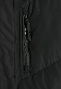 Czarna kurtka z zamykanym na zamek kieszonką z teksturowanym uchwytem, detalami szycia i gładką tkaniną. Logo jest subtelnie wytłoczone.