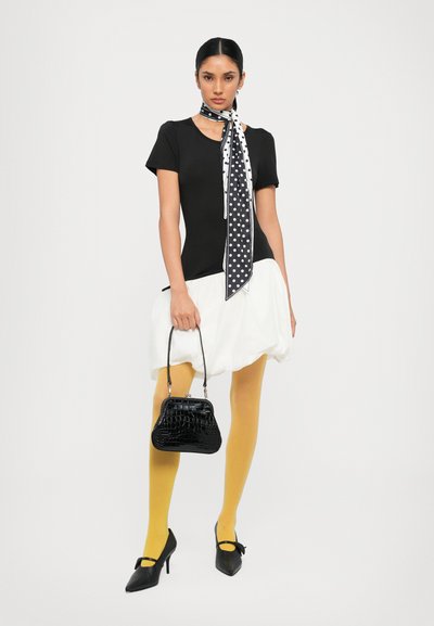Zwarte aansluitende top, witte volumineuze rok, mosterdgele panty, zwarte hakken met strikken, polka dot sjaal en een gestructureerde zwarte handtas.