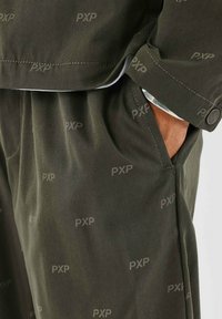 Pantalones de tela verde oscuro con una textura suave, que presentan un sutil patrón de logo PXP y bolsillos laterales. Ajuste entallado con diseño de puños.
