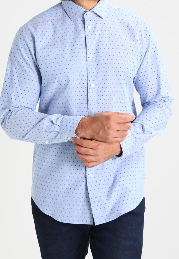 Camisa de botones azul claro con pequeños lunares azul oscuro, de manga larga y cuello extendido. El tejido parece suave y ligero.