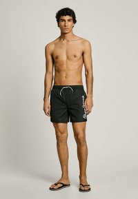 Μαύρο μαγιό με κορδόνι στη μέση, διακοσμημένο με λευκό κείμενο στο πλάι, κατασκευασμένο από ελαφρύ, γρήγορο σε στέγνωμα υλικό.