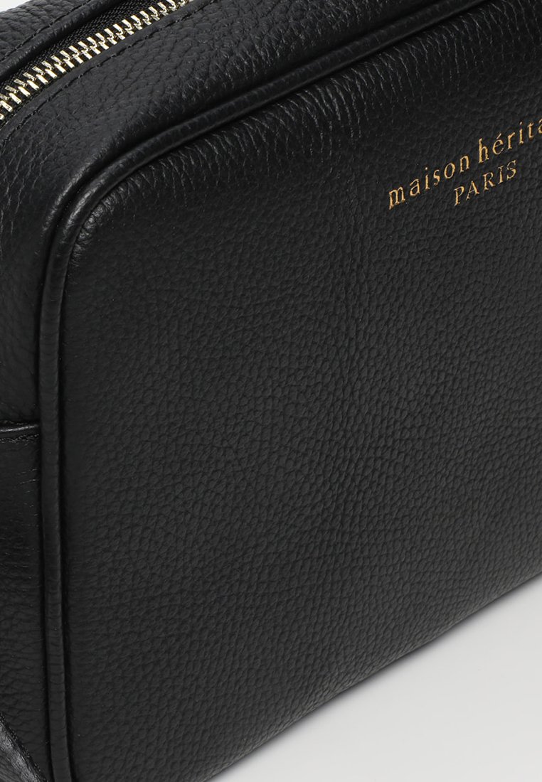 Borsa da toiletta in pelle nera con finitura testurizzata, caratterizzata da un nome del brand "maison héritage PARIS" in oro stampato a caldo e una chiusura con zip.