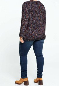 Texturerad svart tröja med flerfärgade fläckar, långa ärmar och rund halsringning. Bärs med mörkblå skinny jeans och beige klackboots.