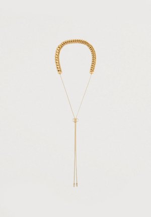 Χρυσή αλυσίδα με χοντρή αλυσίδα από πάνω, λεπτή ρυθμιζόμενη αλυσίδα από κάτω και μια μικρή λεπτομέρεια λογότυπου που συνδέει τα δύο τμήματα.