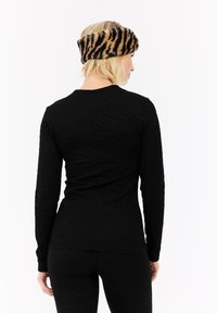 Zwarte top met lange mouwen en een gestructureerd patroon, gecombineerd met zwarte legging. Een bruine en zwarte gestreepte nepbont haarband maakt de look compleet.